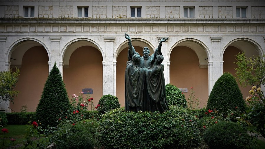 Pomnik rzeźbiarski w ogrodzie klasztoru na Monte Cassino na tle krużganków z arkadami