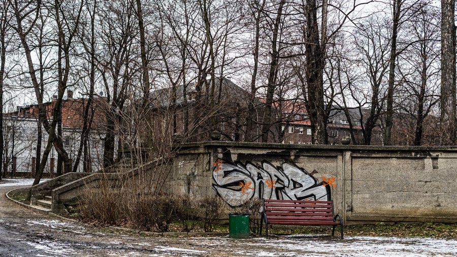 Ławka i grafitti na murze oporowym w zimowym Parku Dubiela w Zabrzu