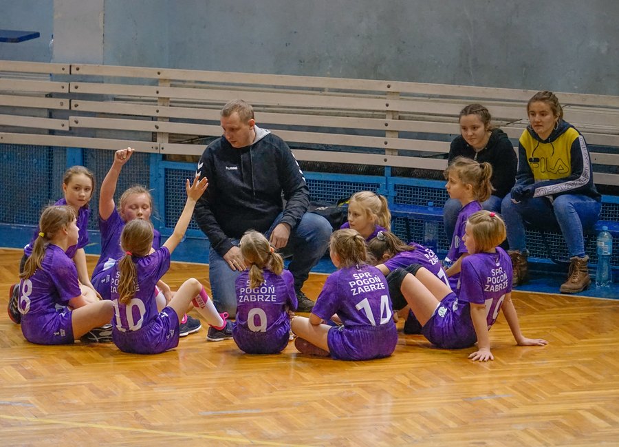 Trener omawia taktykę z drużyną dziewcząt SPR Pogoń Zabrze siedzącą na parkiecie