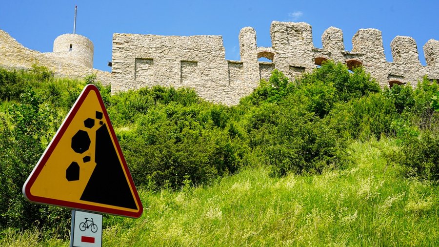 Znak ostrzegawczy przed osuwającymi się kamieniami na tle murów ruin Zamku Rabsztyn